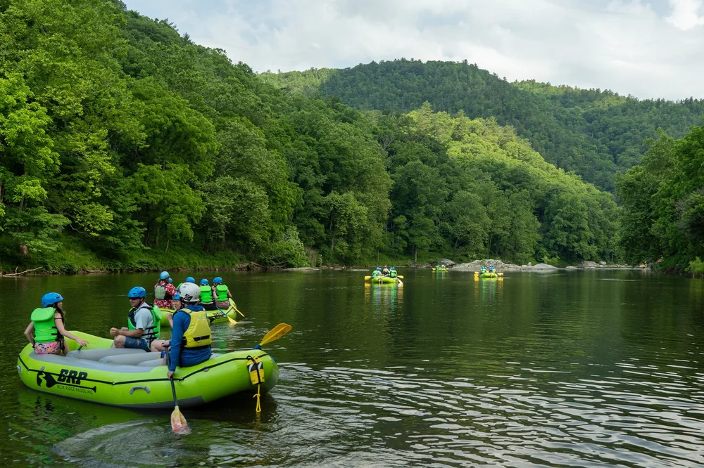 Guided rafting groups floating on the Nolichucky River beneath forested mountains
